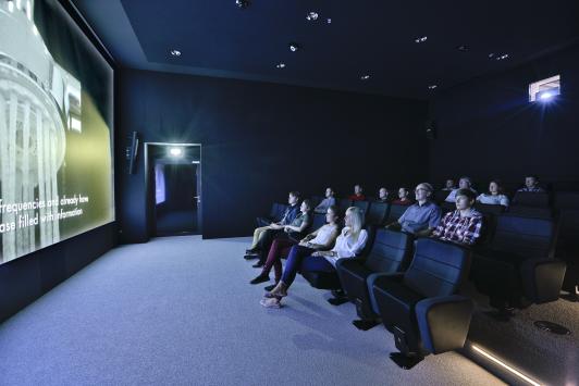Kinoraum in der Hansgrohe Aquademie Schiltach mit Besuchern, die eine Präsentation oder einen Film auf großer Leinwand verfolgen