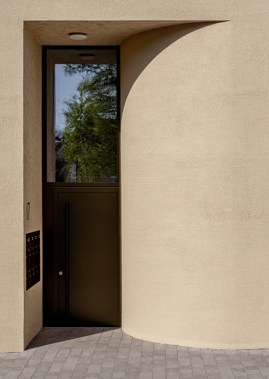 Eingangsbereich eines Wohngebäudes mit strukturierter Putzfassade, gerundeter Wand und dunkler Tür mit Glasöffnung geplant und umgesetzt von arc+ Freudenstadt
