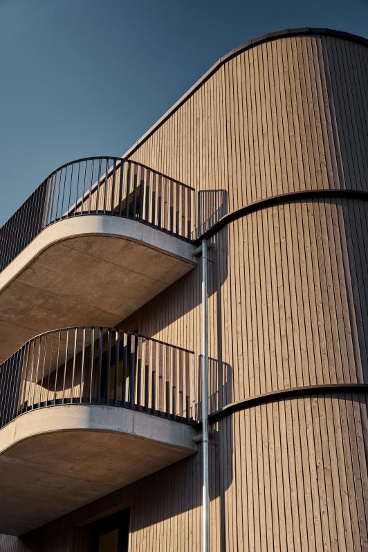 Detailansicht einer Wohnanlage mit geschwungenen Balkonen und vertikaler Holzfassade
