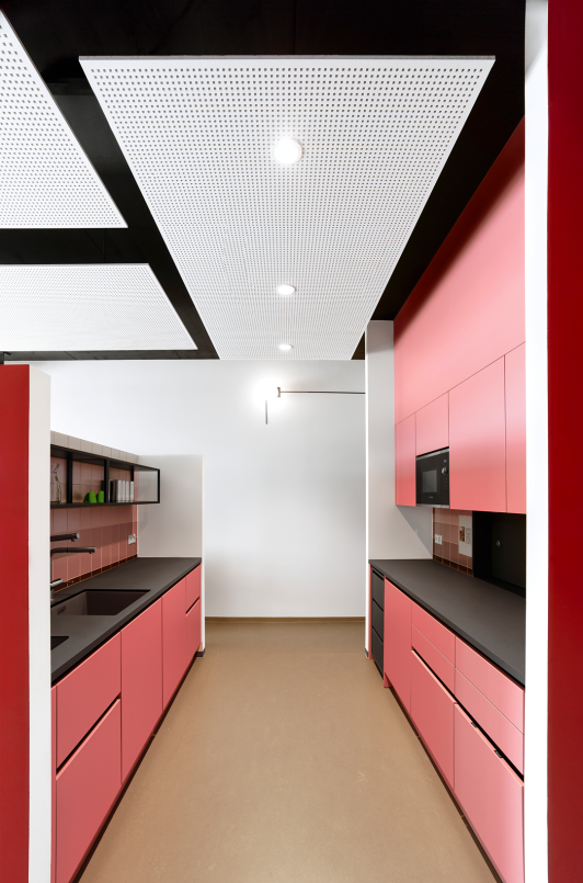 Moderne Teeküche im Verwaltungsbau Gläser in Horb mit roten Einbaumöbeln, schwarzer Arbeitsplatte und klarer Gestaltung. Architektur arcplus Freudenstadt