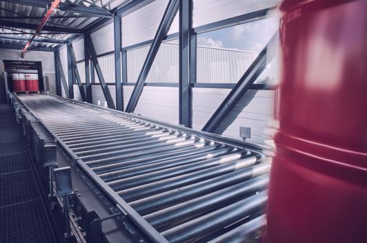 Innenansicht der Logistikbrücke im Projekt Oest mit integrierter Fördertechnik als direkte Schnittstelle zwischen Produktions- und Versandbereich – geplant und umgesetzt von arc+
