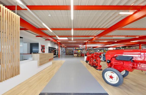 Offener Eingangs- und Ausstellungsbereich des Unternehmens Ziegler mit Empfang, Verkaufsfläche und Präsentation historischer Landtechnik. geplant und umgesetzt arc+ Freudenstadt