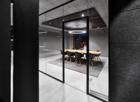 Blick in den Besprechungsraum des Bürogebäudes ›Büro am Stadtbahnhof‹ mit gläserner Raumabtrennung, zentralem Konferenztisch und gezielter Lichtgestaltung, geplant und realisiert von arc+ Architekten als eigenes Büro in Freudenstadt